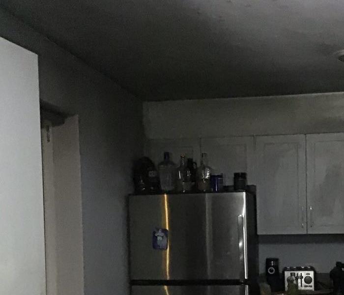 a kitchen affected with black soot with a fridge next to a wall 