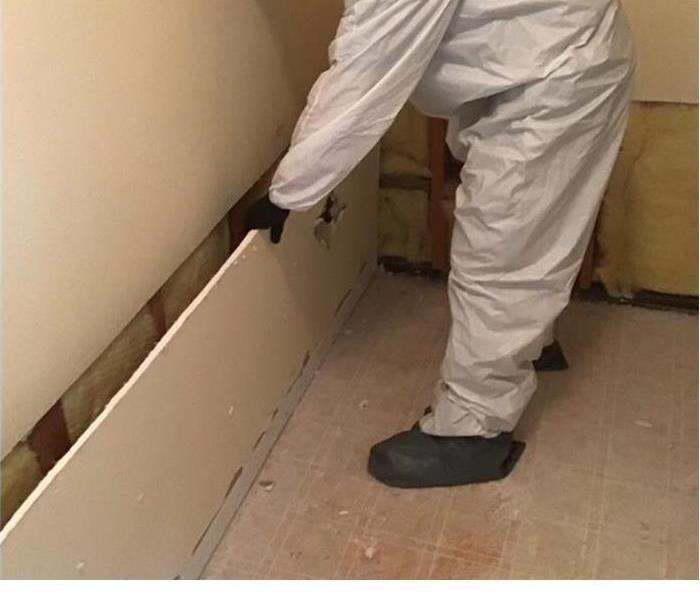 Servpro technician with a suit on removing a piece of drywall