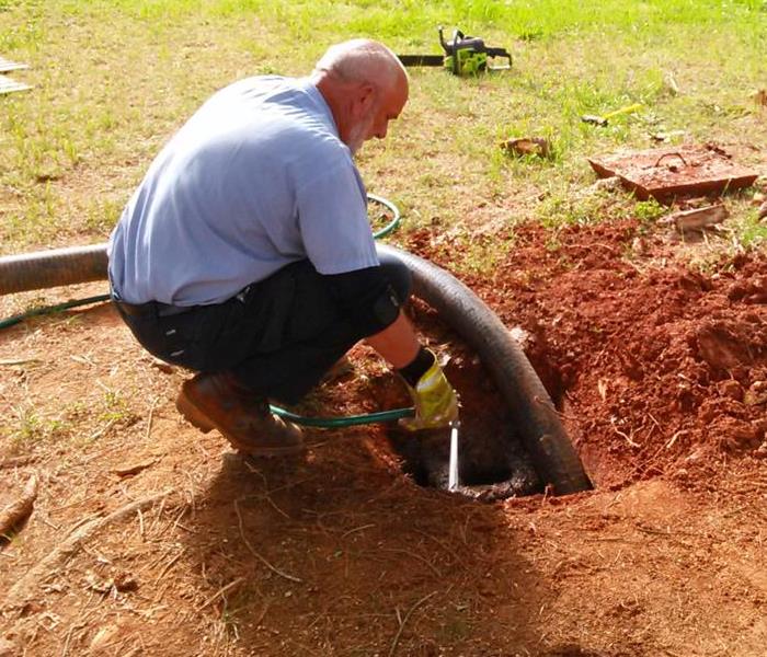 Man holding a tube inserted in the ground where the septic tank is located