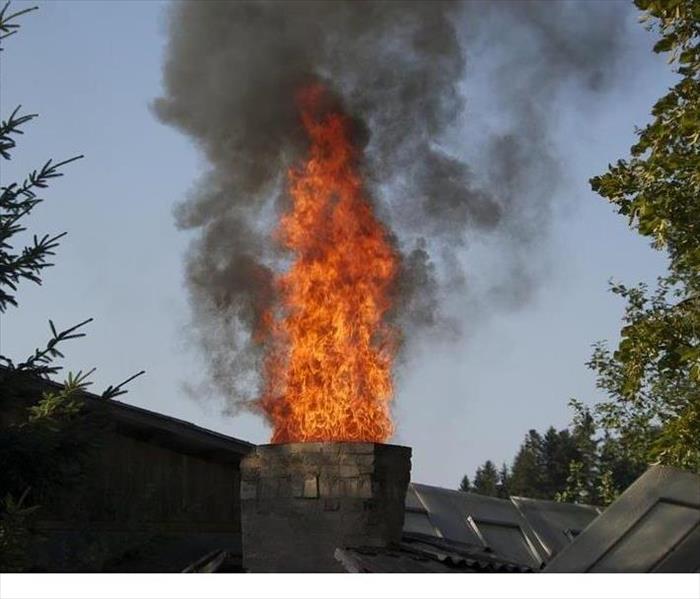 A chimney up in flames surrounded by two trees